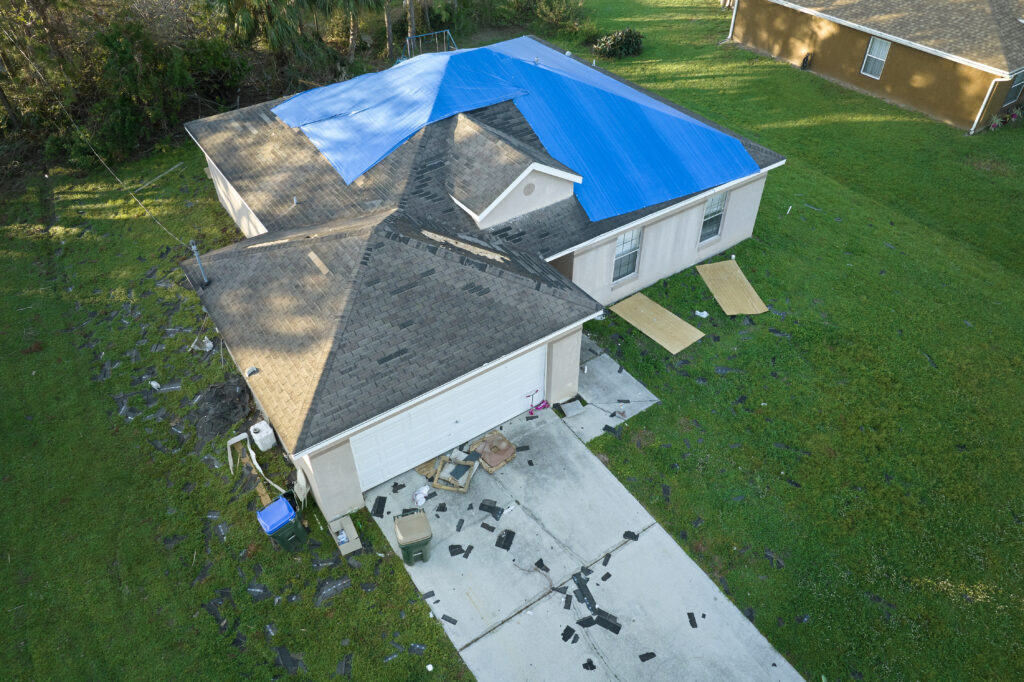 Storm Season Cleanup Made Easier with a Dumpster Rental 1 Top view of leaking house roof covered with protective tarp sheets against rain water leaks until replacement of asphalt shingles